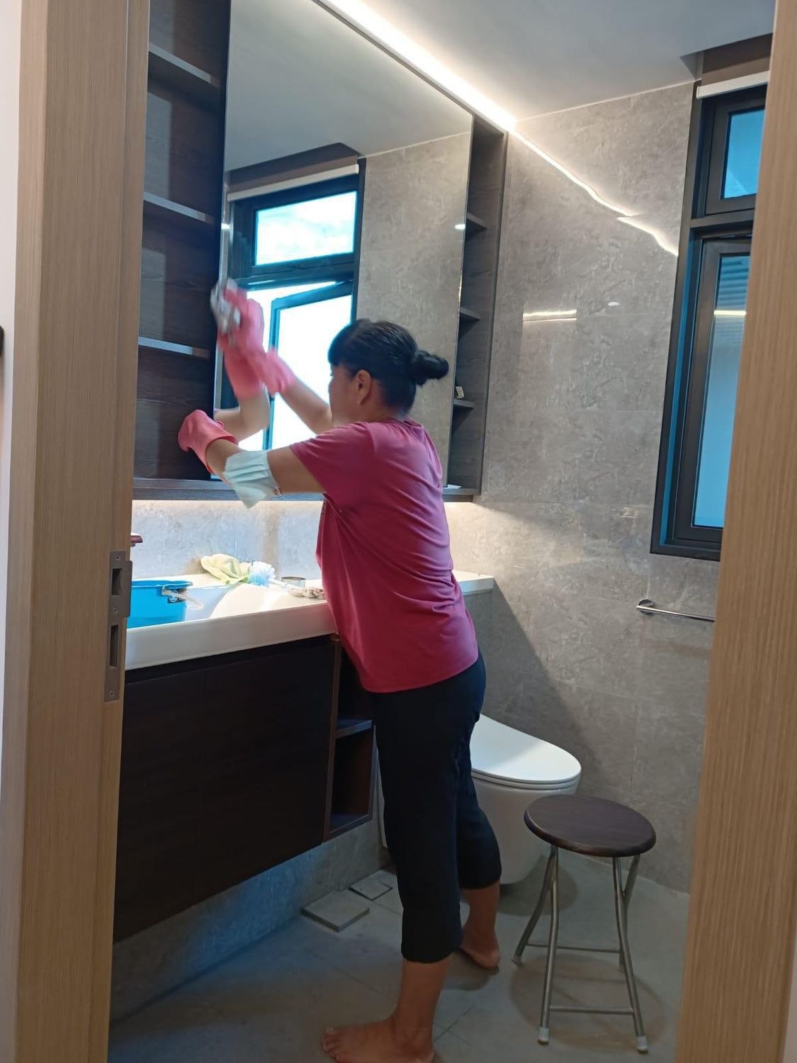 Cleaner sanitising a washroom mirror and vanity